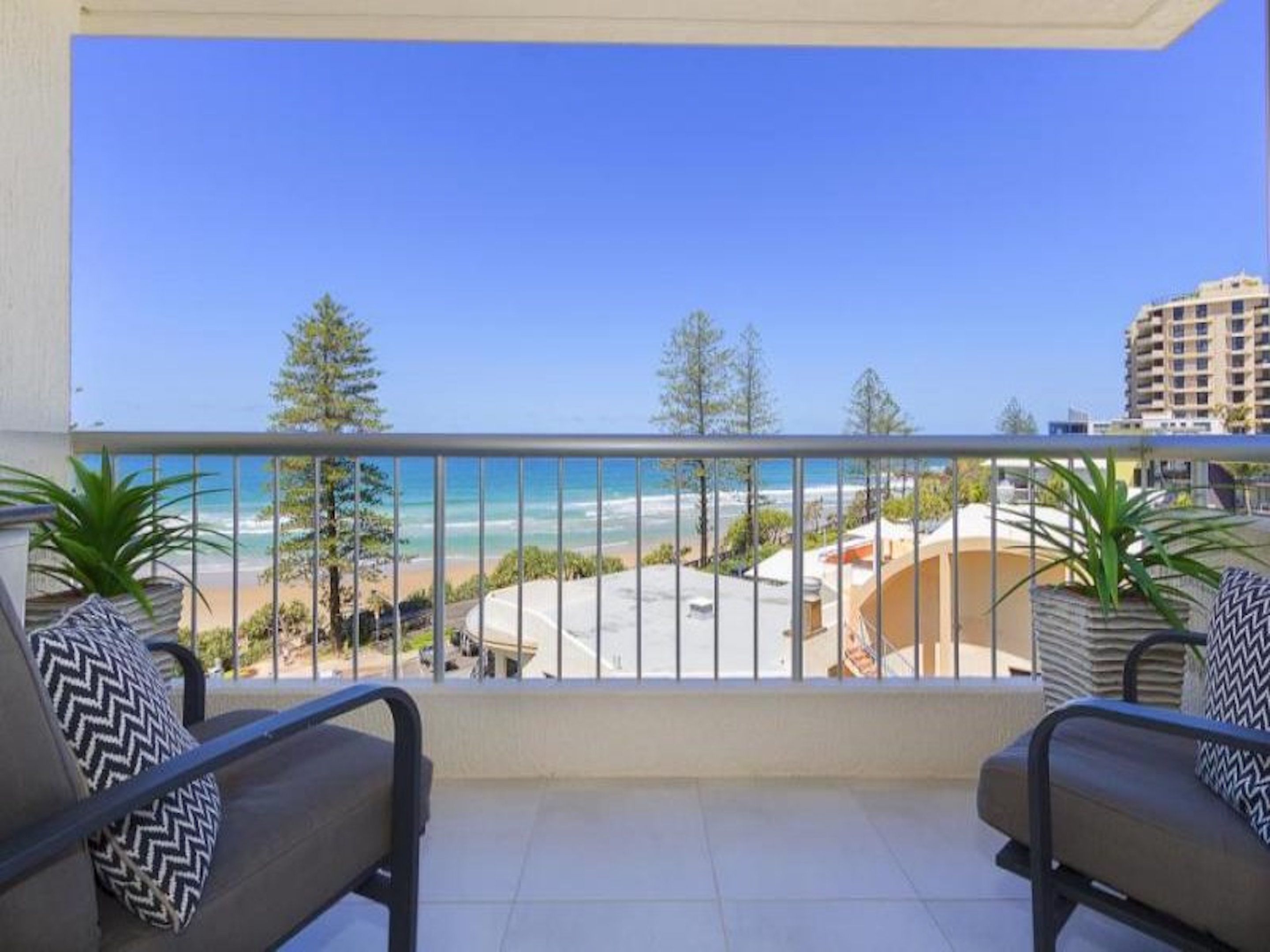 A balcony with a view of the beach and ocean, two chairs with patterned cushions, and a railing.