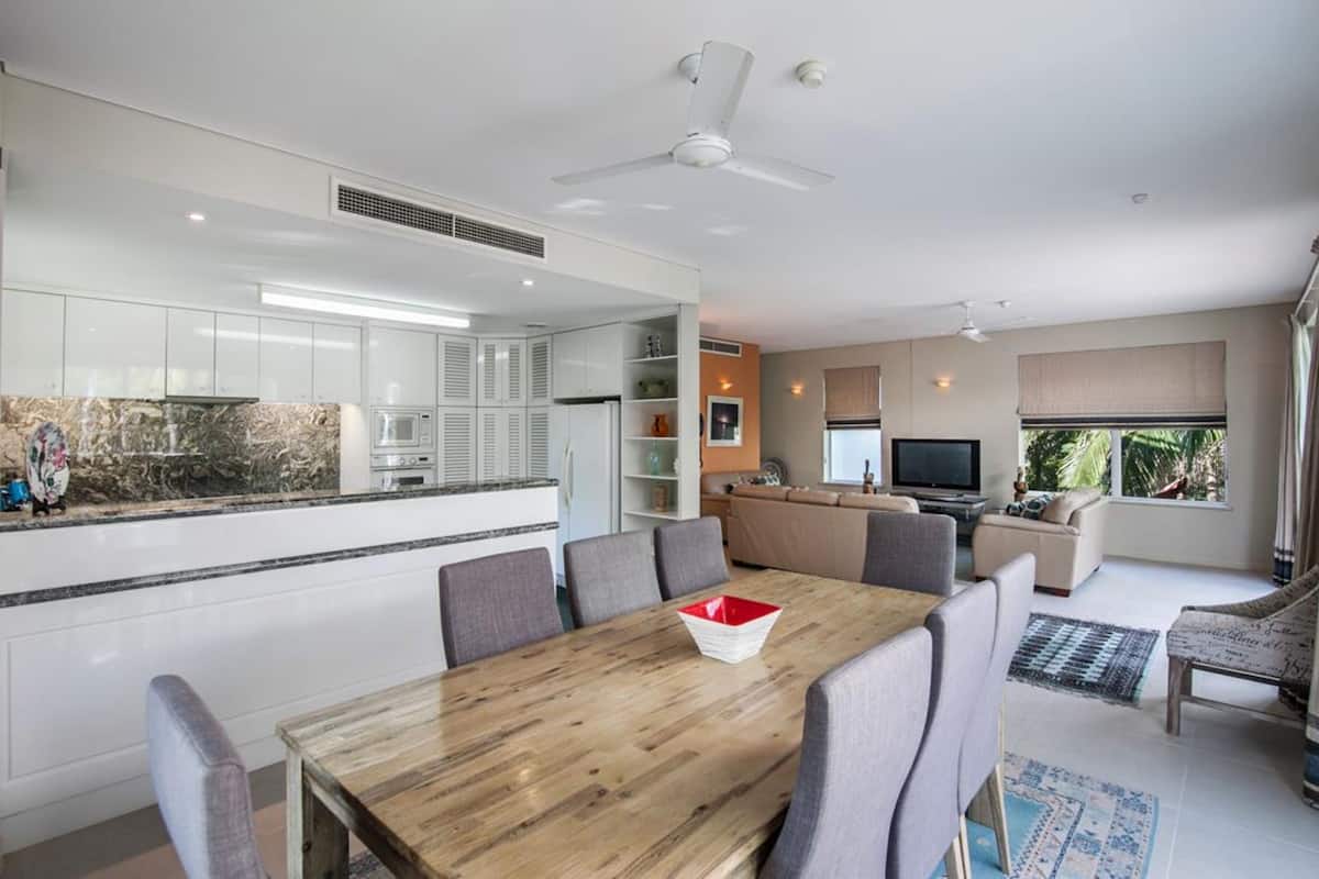 A modern kitchen with white cabinets, a marble countertop, and a dining area with a wooden table and chairs.