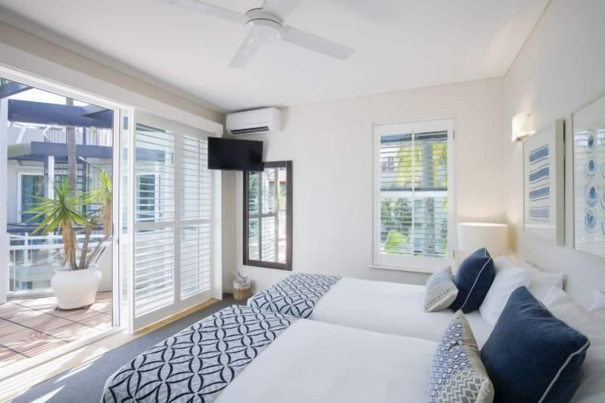 A bedroom with a bed, a ceiling fan, a TV, and a window with blinds.