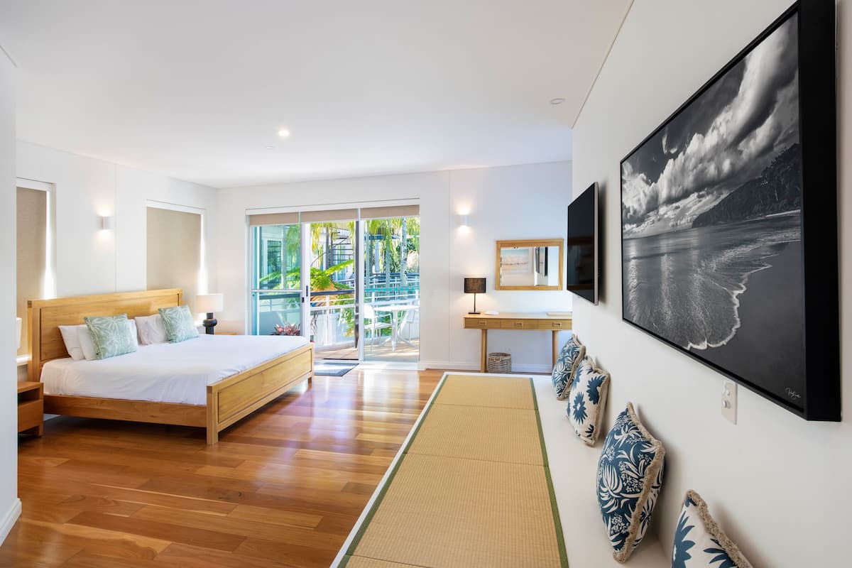 A modern bedroom with a wooden bed, a desk, and a large window with a view of greenery.