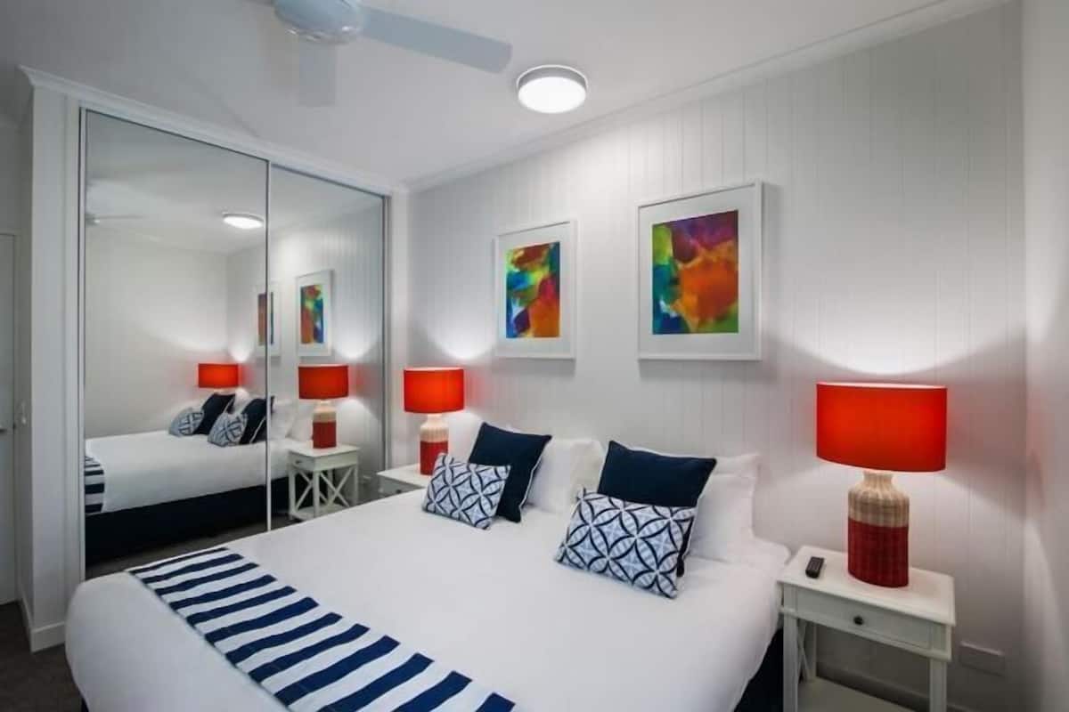 A hotel room with a large bed, two bedside tables, a mirror, and abstract wall art.