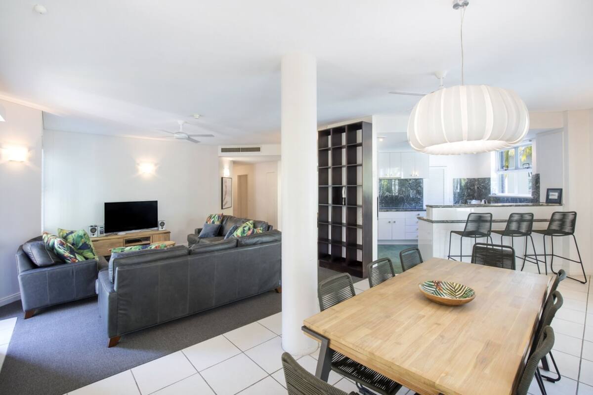A modern living room with a grey sofa, a flat-screen TV, and a dining area with a wooden table and chairs.