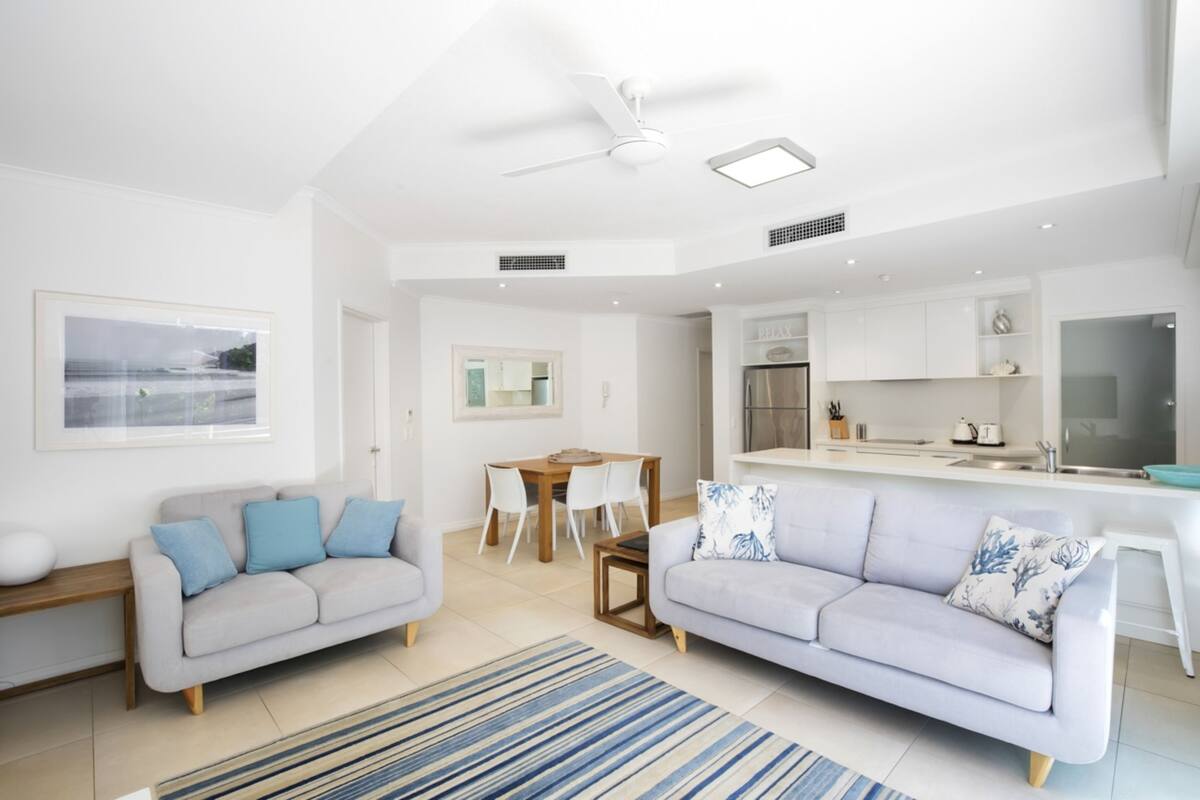 A modern living room with two sofas, a dining table, and a kitchen area.