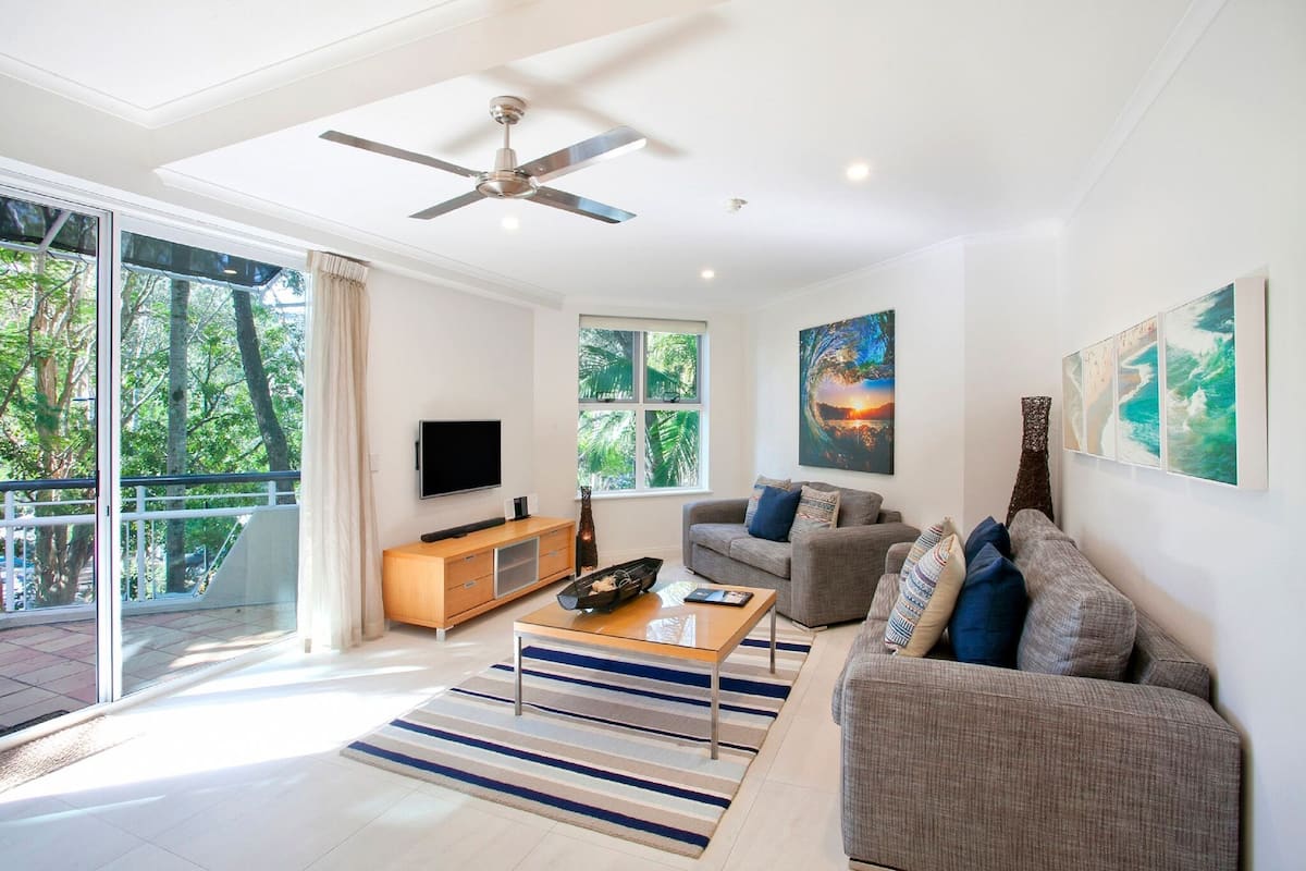 A modern living room with a flat-screen TV, a sofa, a coffee table, and artwork on the walls.