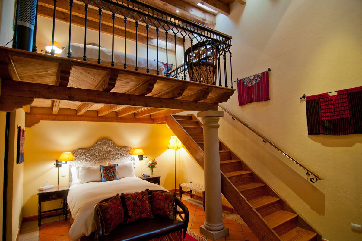 A bedroom with a large bed, a wooden staircase, and a balcony with a railing.