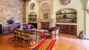 Un interior rústico con pared de piedra, muebles de madera, chimenea y estantes con adornos.