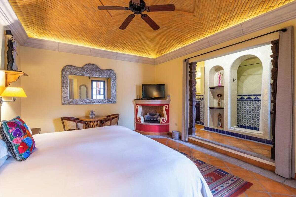A hotel room with a large bed, a television, a fireplace, and a view of a courtyard with arches.