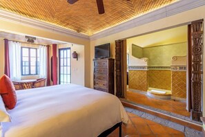 A hotel room with a bed, a TV, a desk, and a bathroom with a shower and tiled walls. - Antigua Capilla B&B (San Miguel de Allende)