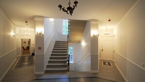 A grand staircase with a chandelier, a patterned floor, and wall sconces. - Crystal Suites Old Town (Kraków)