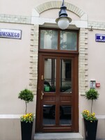 Entrada de un edificio con una puerta marrón, una señal de calle en la parte superior y dos macetas a cada lado.