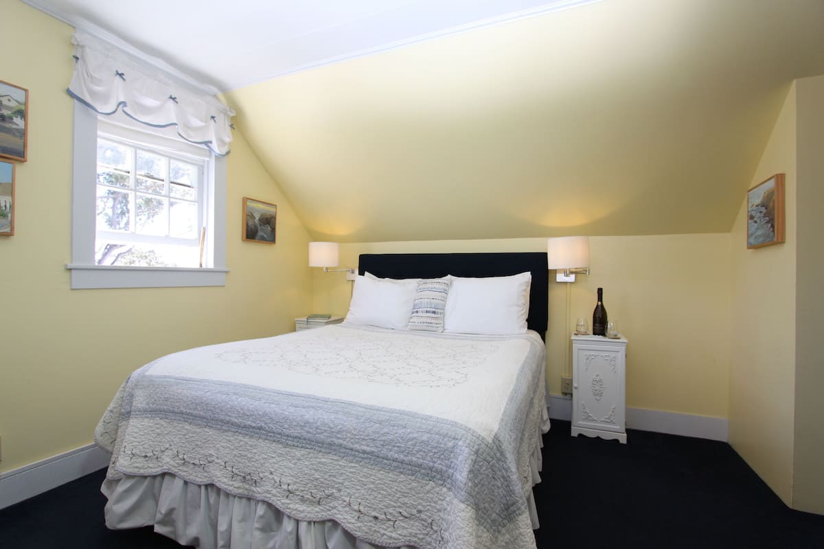 A bedroom with a large bed, two bedside tables, a window with curtains, and a wall-mounted lamp.