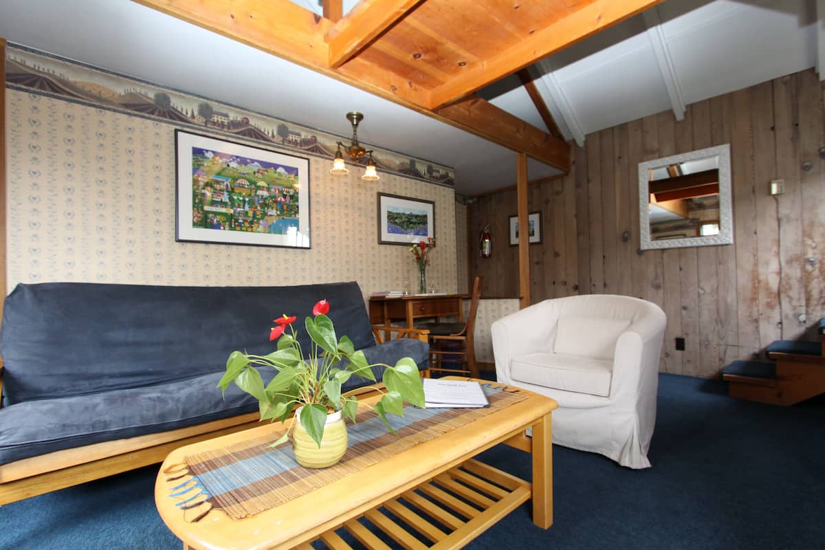 A cozy living room with a sofa, a chair, a wooden coffee table with a plant, and framed pictures on the wall.
