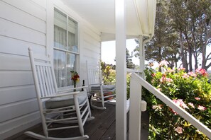 A porch with white rocking chairs and a small table with a vase of flowers.