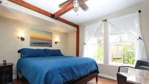 A bedroom with a bed, a desk, a chair, a ceiling fan, and a window with curtains. - Seagull Inn (Mendocino)