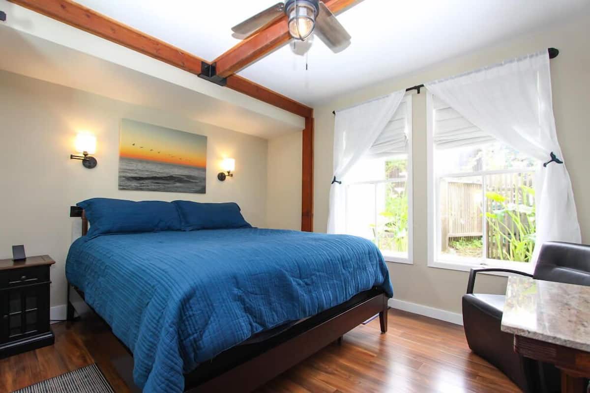A bedroom with a bed, a desk, a chair, a ceiling fan, and a window with curtains.