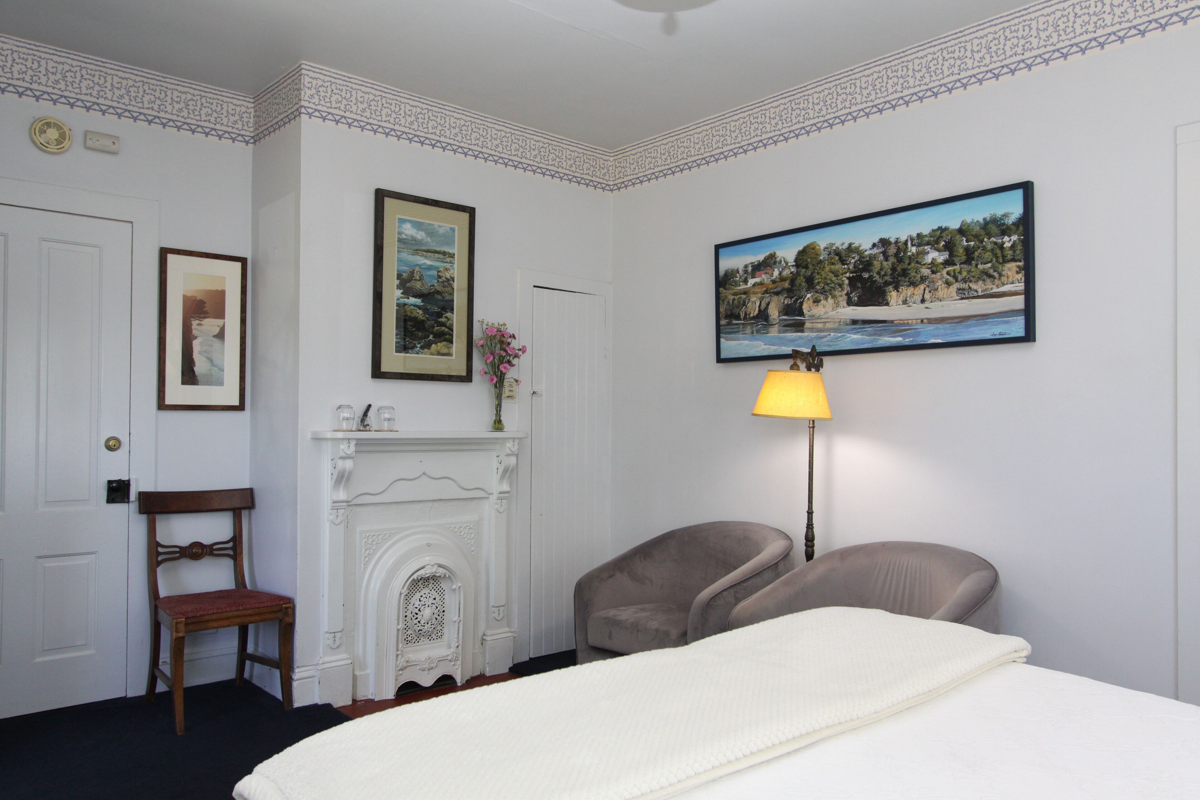 A hotel room with a bed, a fireplace, a chair, a lamp, and a painting on the wall.