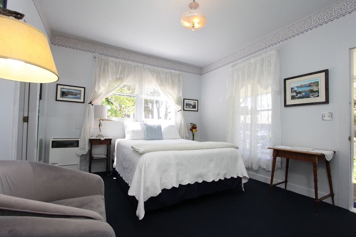 A bedroom with a bed, a bedside table, a chair, and a window with curtains.