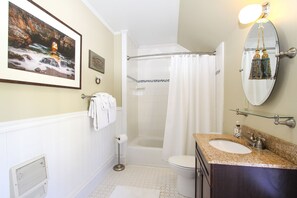 Bathroom features a large framed picture, white bathtub, toilet, and granite sink with modern faucet.