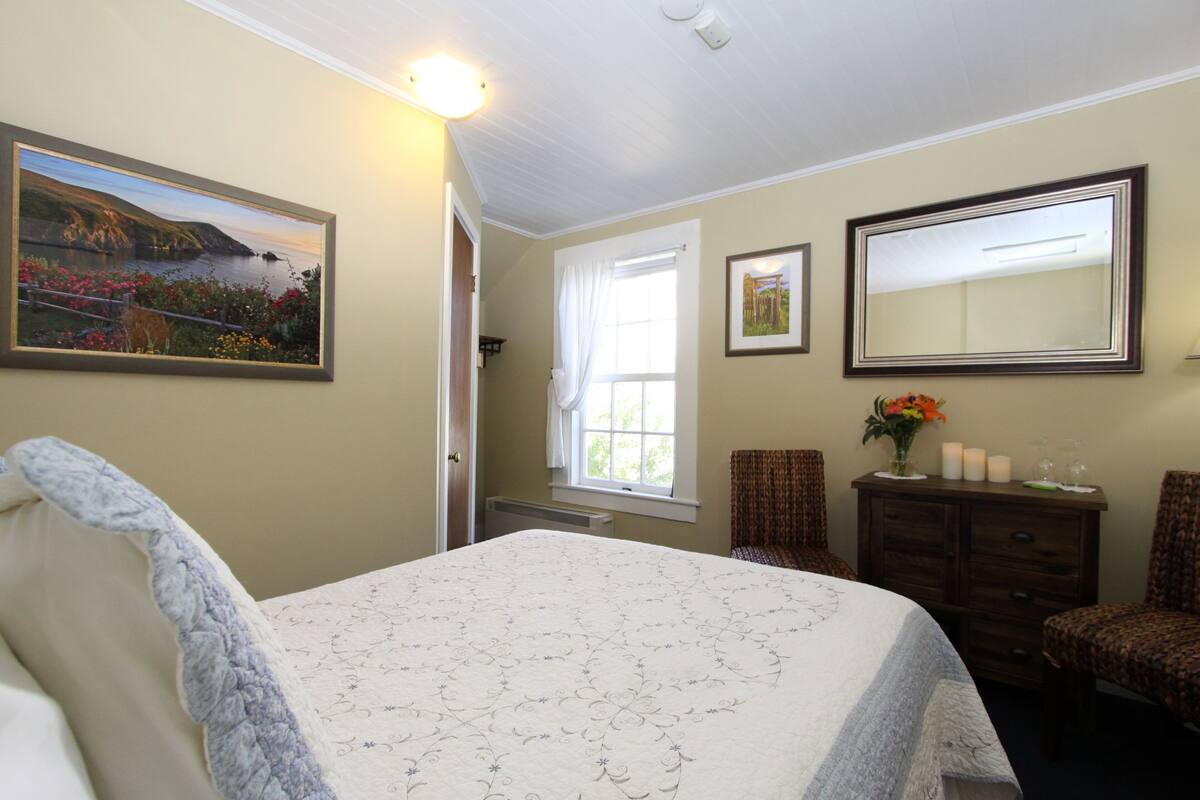A bedroom with a bed, a dresser, a mirror, and a window with curtains.