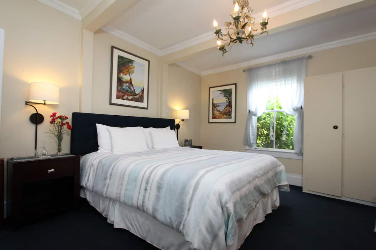 A neatly arranged bedroom with a large bed, two bedside tables, a chandelier, and two framed pictures on the walls.