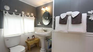 A bathroom with a toilet, sink, and mirror. There are towels hanging on a rack and a small table with a basket.