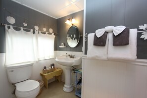 A bathroom with a toilet, sink, and mirror. There are towels hanging on a rack and a small table with a basket.