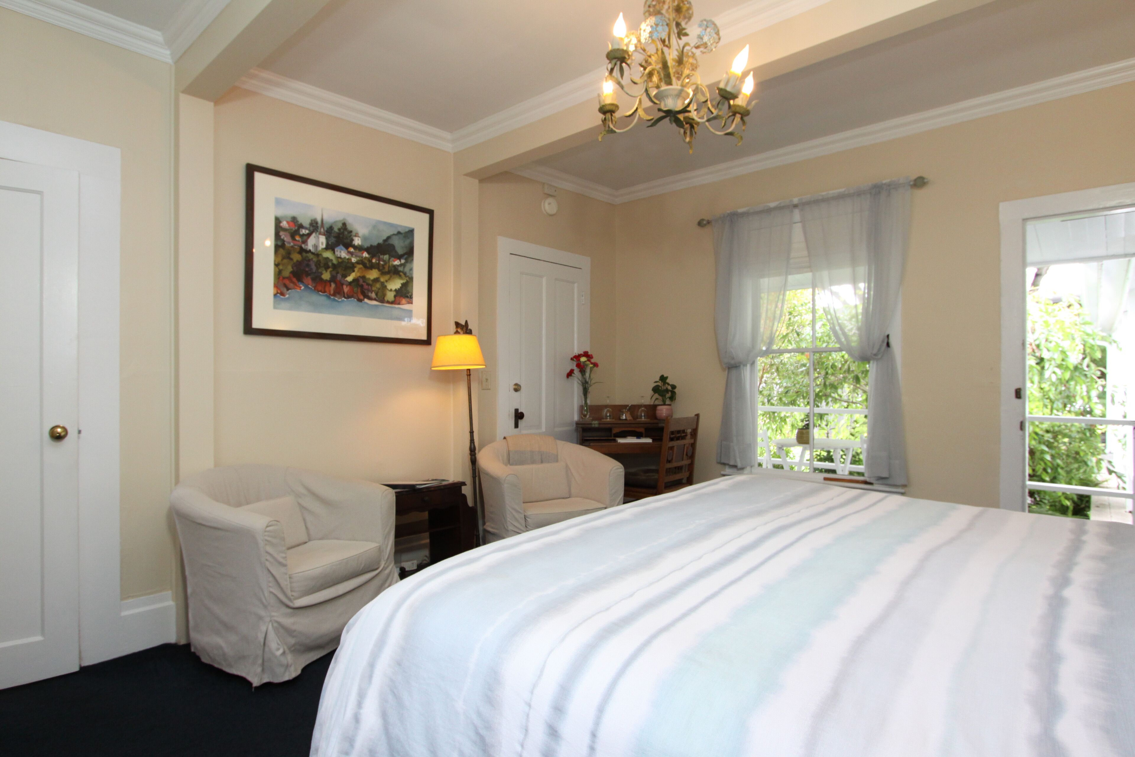 Ein Hotelzimmer mit einem großen Bett, zwei Sessel, einem Schreibtisch, einer Lampe, einem gerahmten Gemälde und einem Fenster mit Vorhängen.