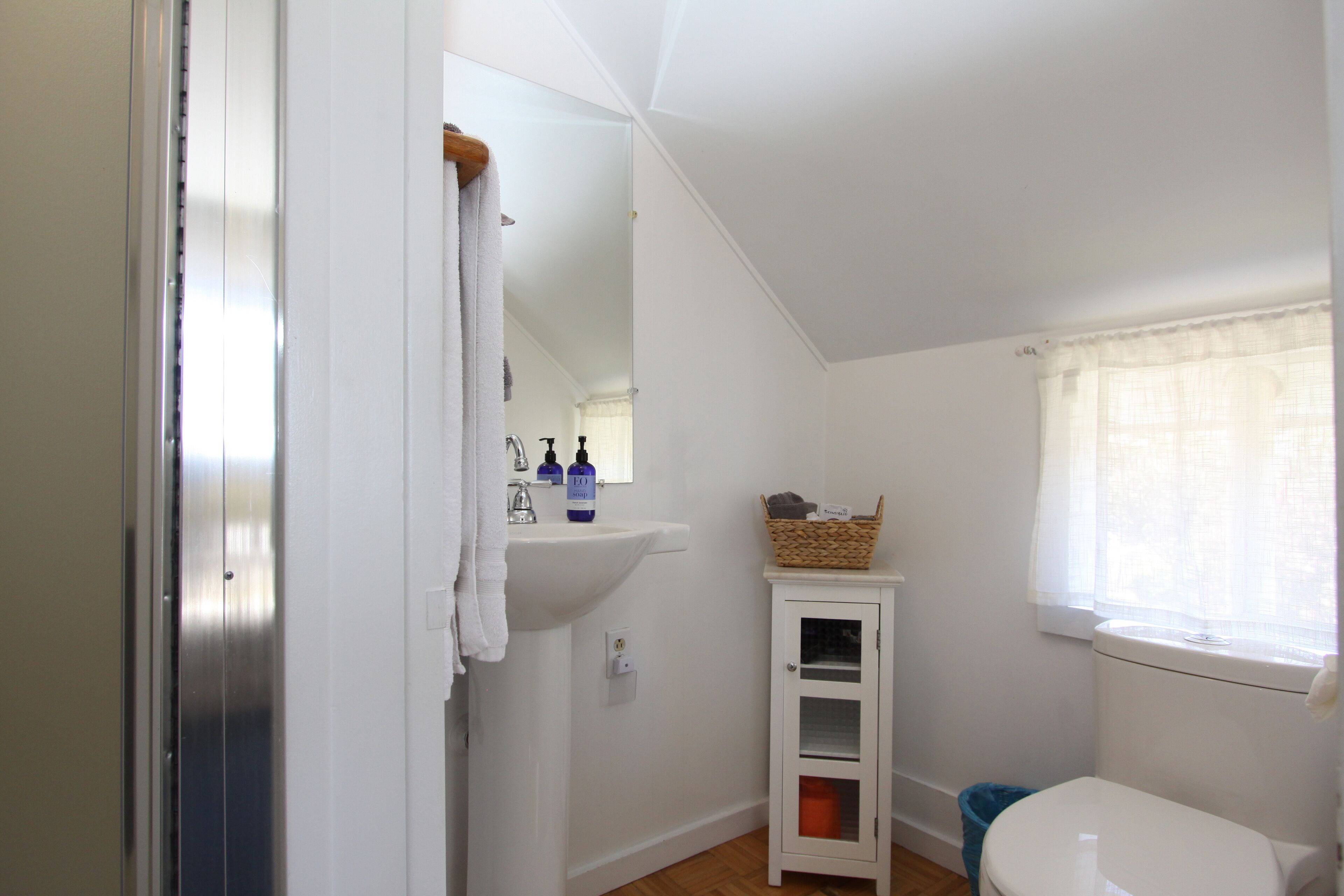 Un baño pequeño y blanco con lavamanos, espejo y ventana.