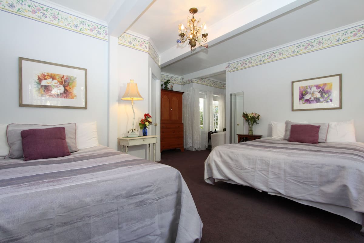 A hotel room with two beds, a desk with a lamp, and a chandelier.