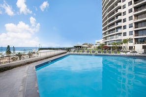 A swimming pool with lounge chairs and a view of the ocean.