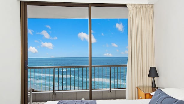 A hotel room with a large window offering a view of the ocean and beach.