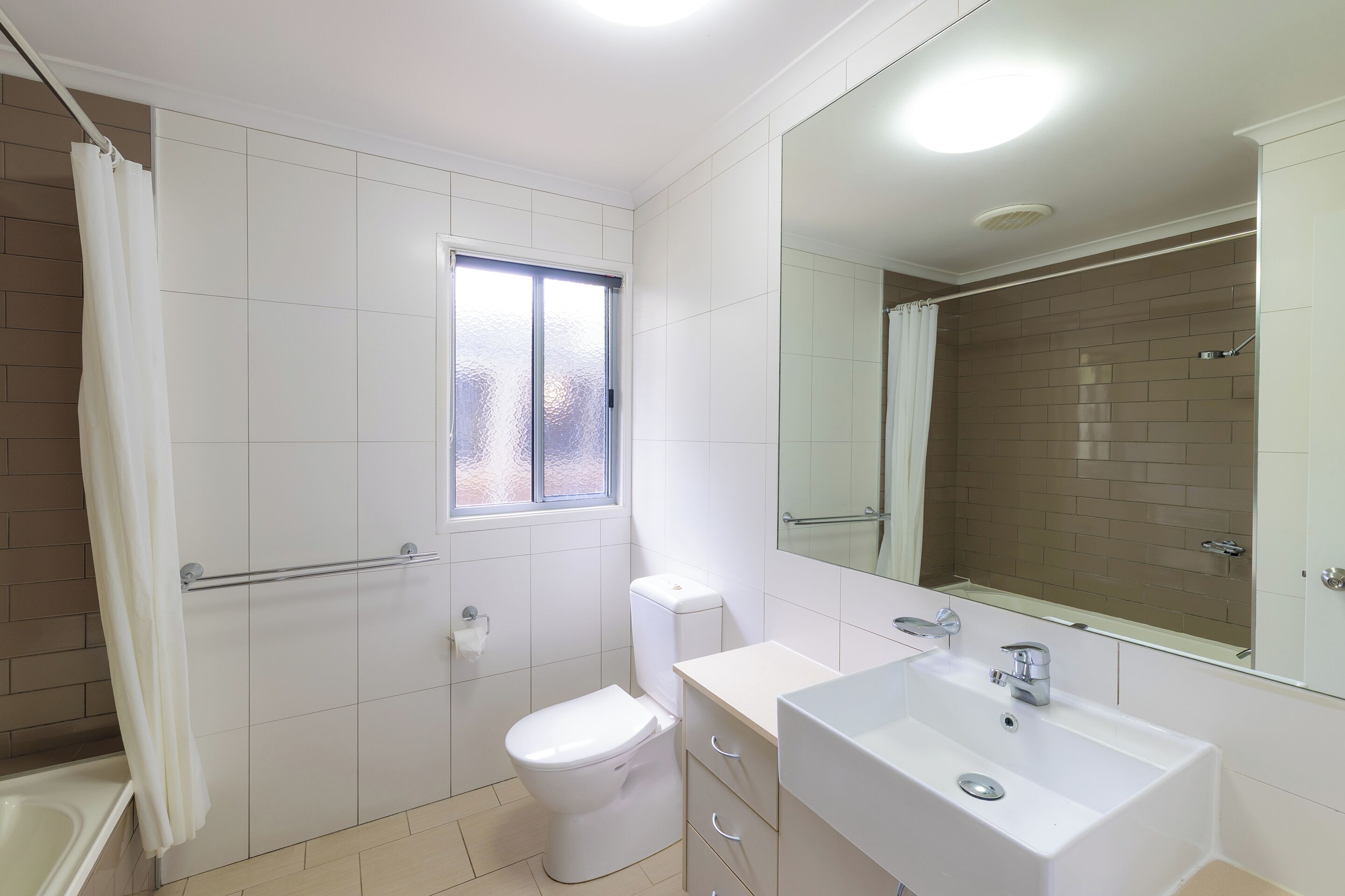 Baño con inodoro, lavabo, espejo y zona de ducha.