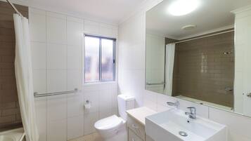 Baño con inodoro, lavabo, espejo y zona de ducha.