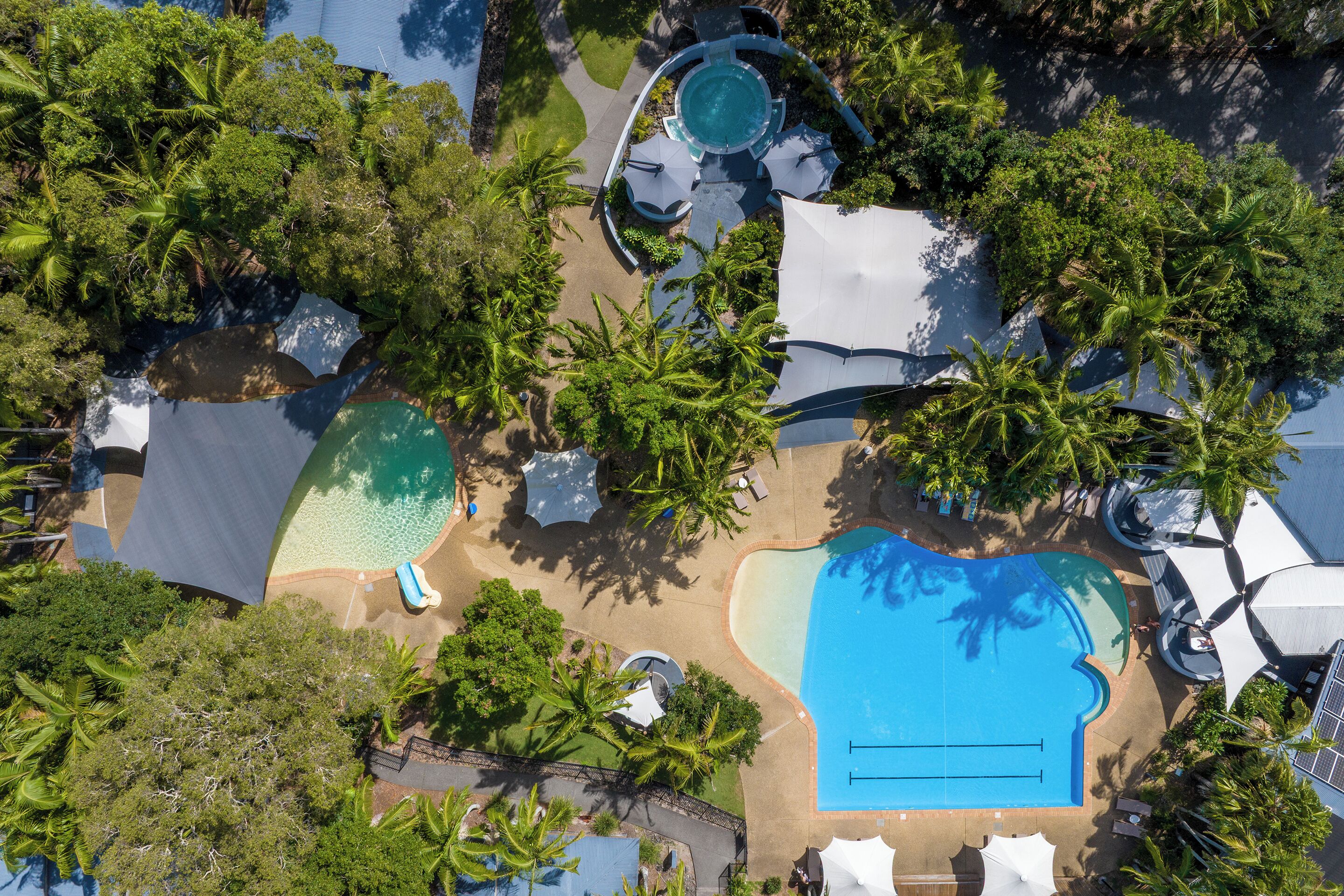 Vue aérienne d’un complexe hôtelier doté de plusieurs piscines, de palmiers et d’espaces ombragés.