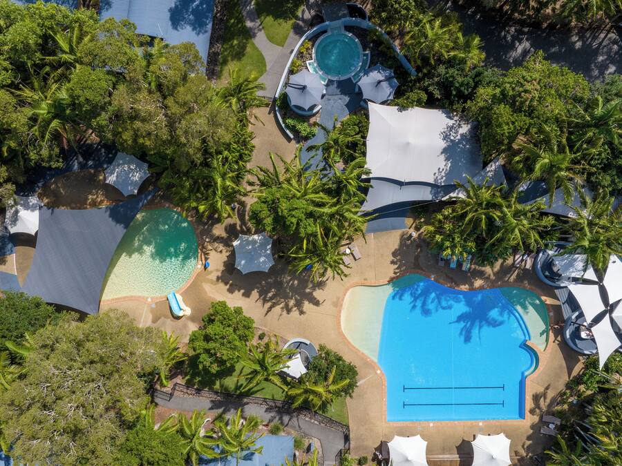 Vue aérienne d’un complexe hôtelier doté de plusieurs piscines, de palmiers et d’espaces ombragés.