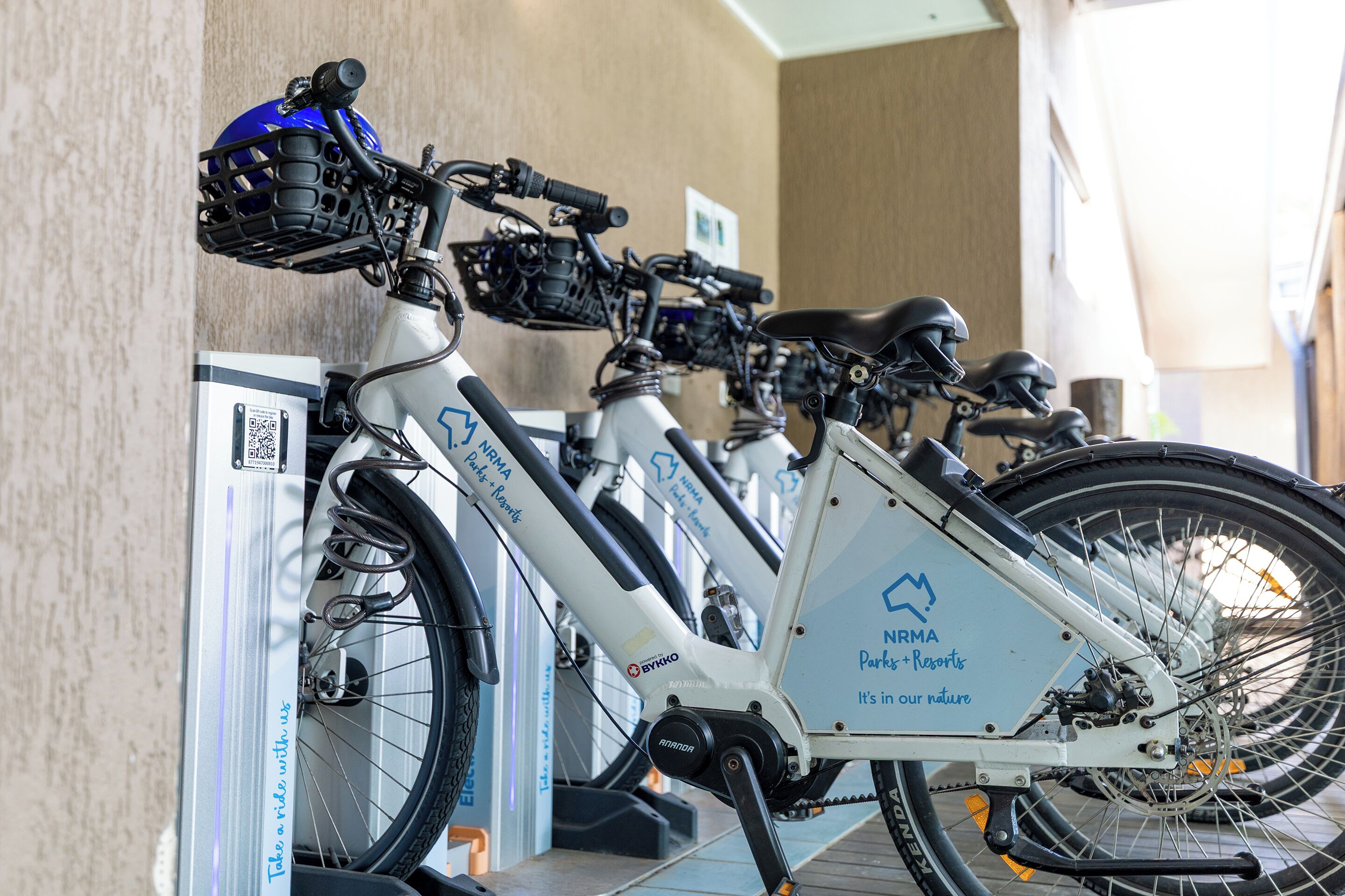 Una fila de bicicletas con cascos y códigos QR estacionadas junto a una pared.