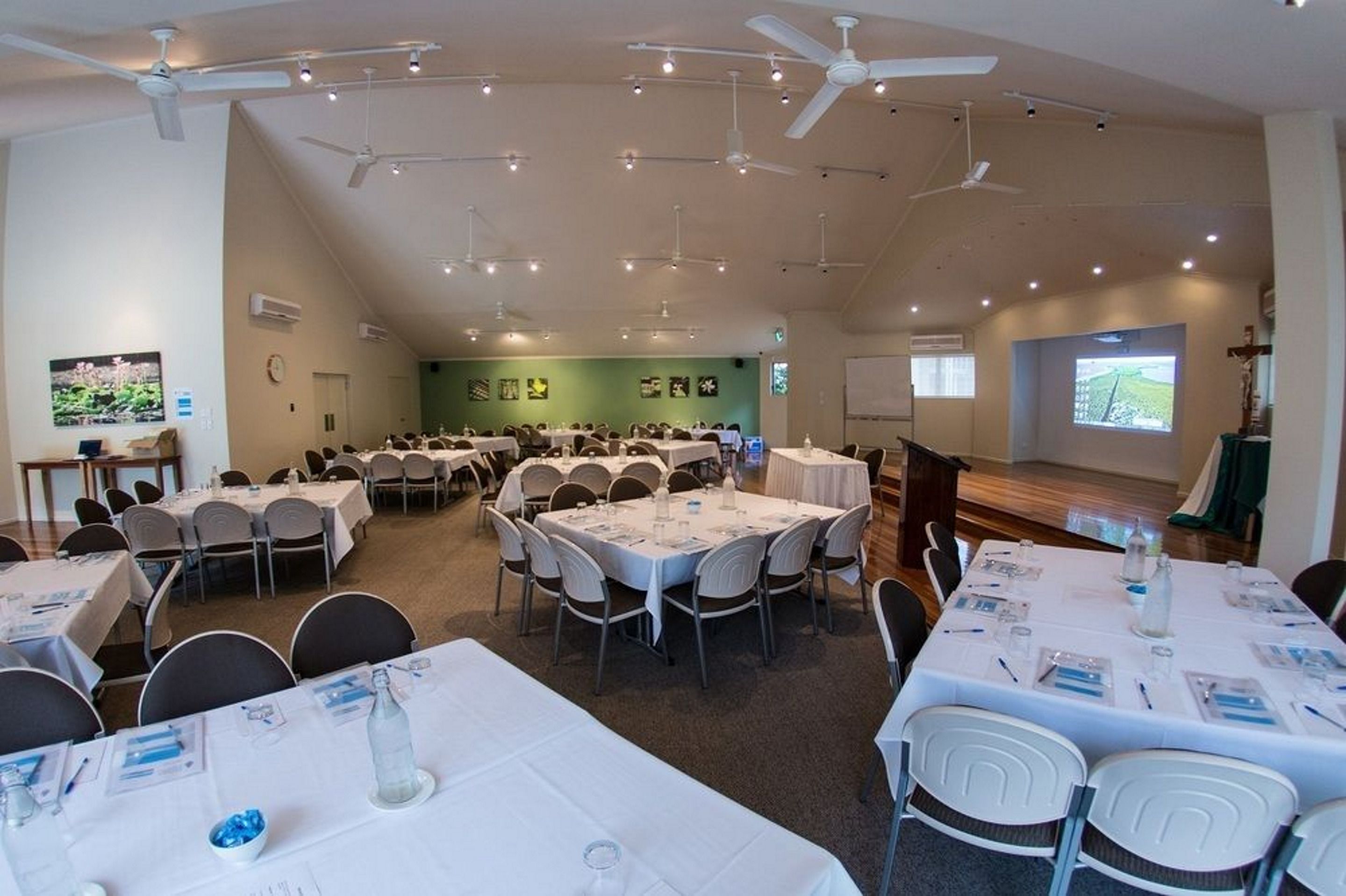 A conference room with multiple tables and chairs, ceiling fans, and a projection screen.