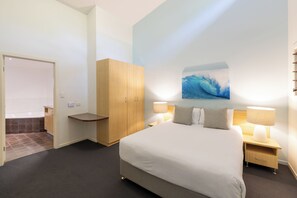 A hotel room with a bed, nightstands, a wooden wardrobe, a bathroom with a bathtub, and a wall-mounted artwork.