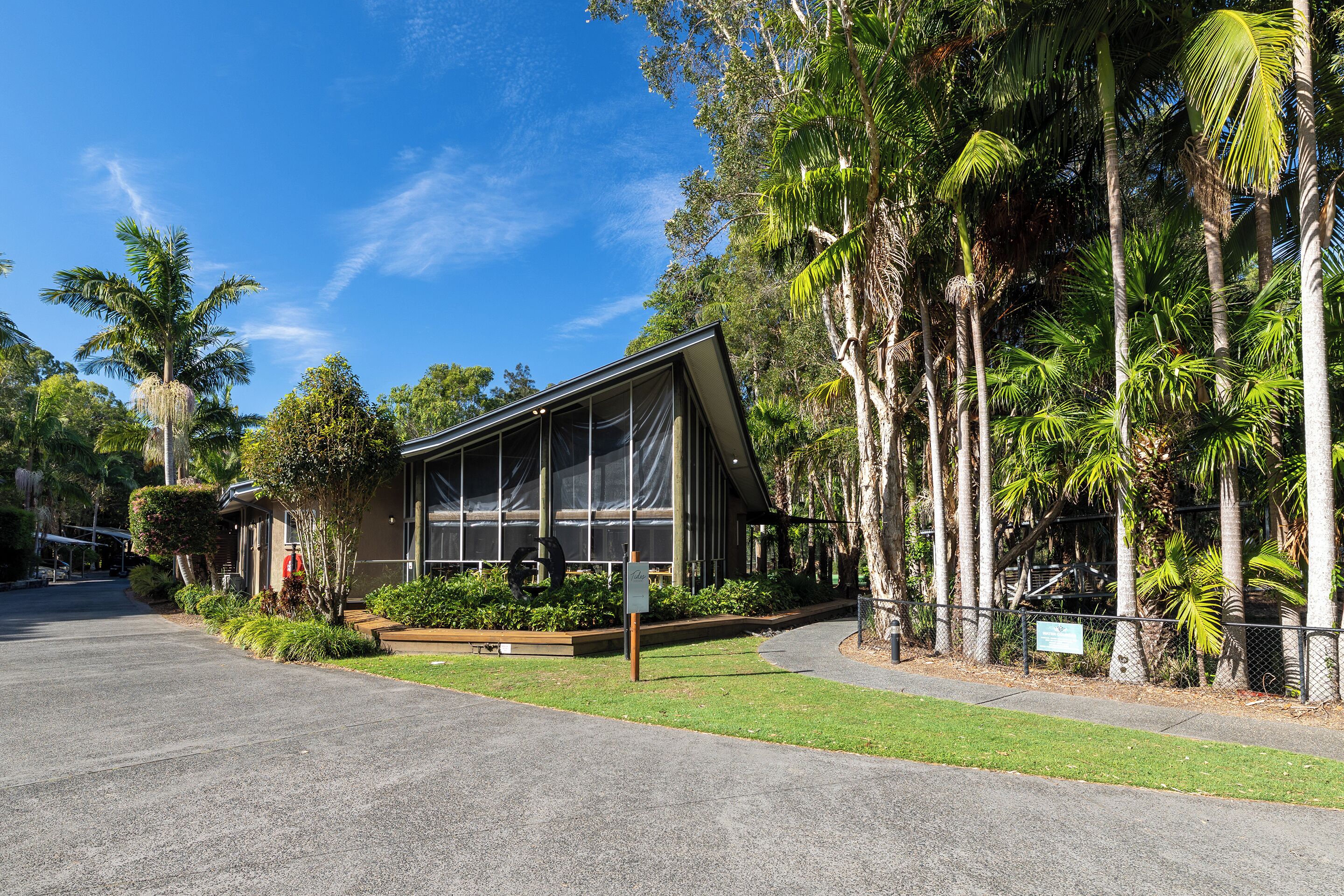 A modern building with large windows, surrounded by lush greenery and palm trees.