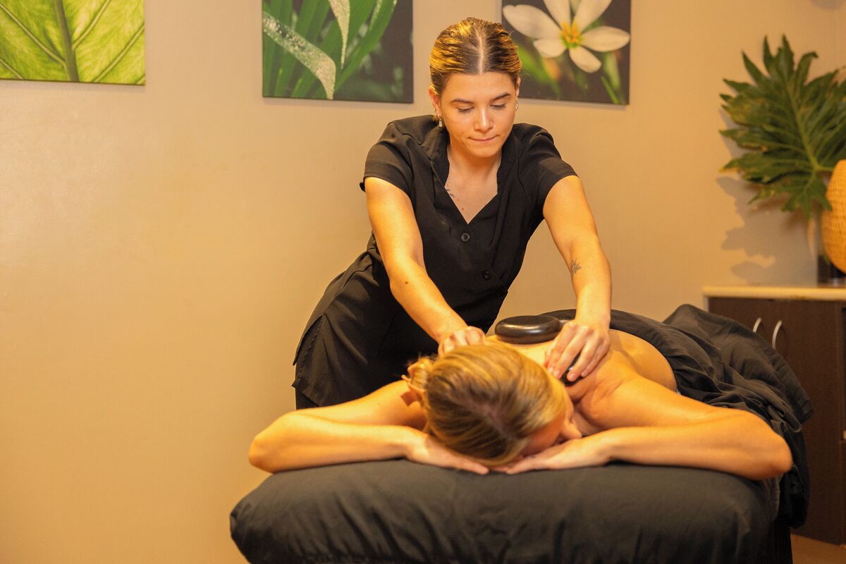 A massage therapy session in a room with a massage table, a wall with framed botanical prints, and a potted plant.