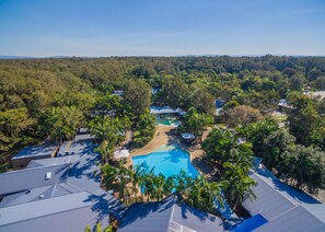 An aerial view of a resort with a central swimming pool surrounded by palm trees and resort buildings.