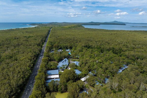 An aerial view of a coastal property with a road, buildings, and surrounding forest.