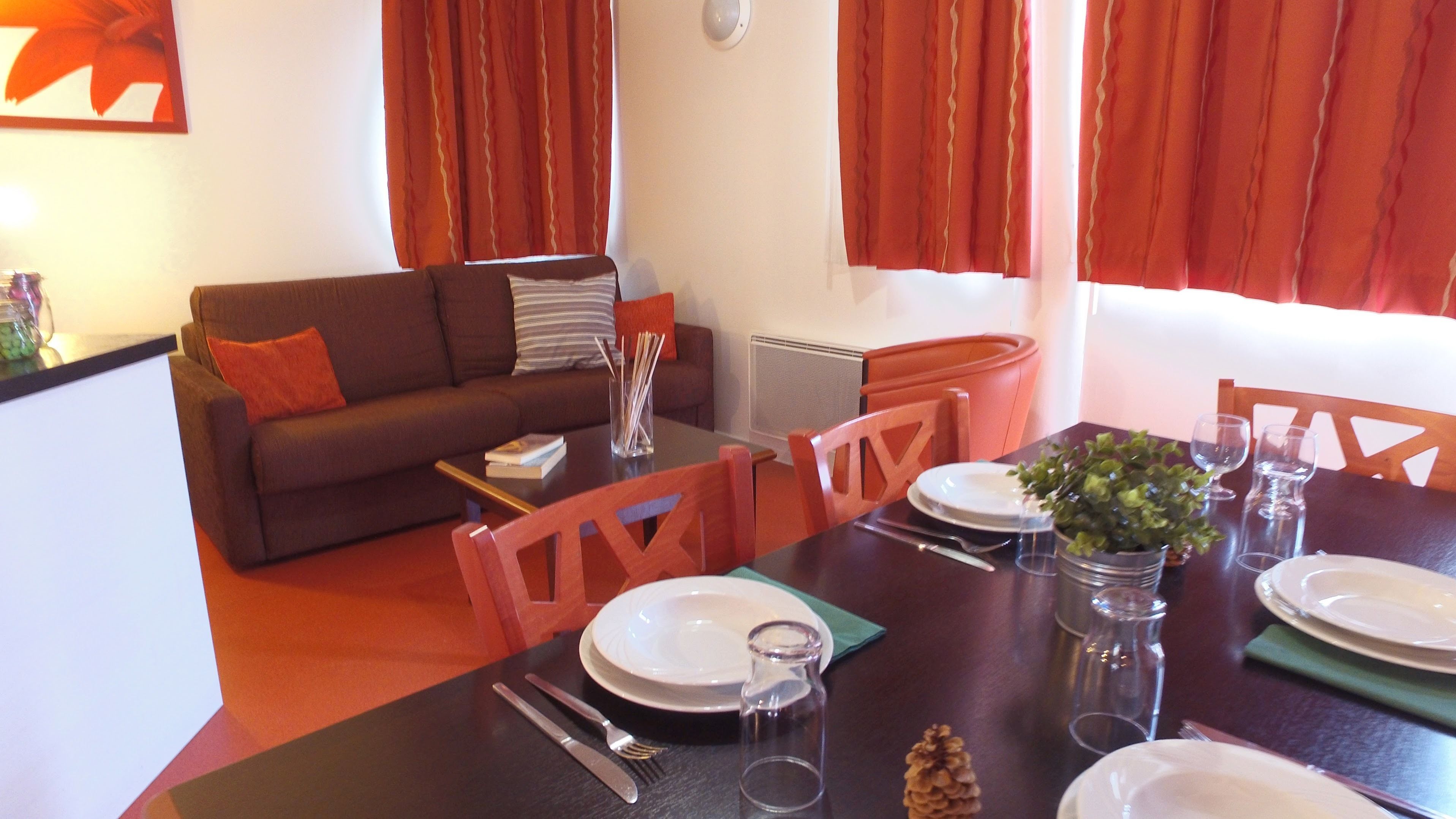 Un coin repas avec une table dressée pour quatre personnes, un canapé et des rideaux rouges.