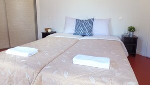 A double bed with a patterned bedspread, two pillows, a bedside table with a lamp, and a small plant on a nightstand. - VVF Gers Gascogne, Mauvezin (Mauvezin)