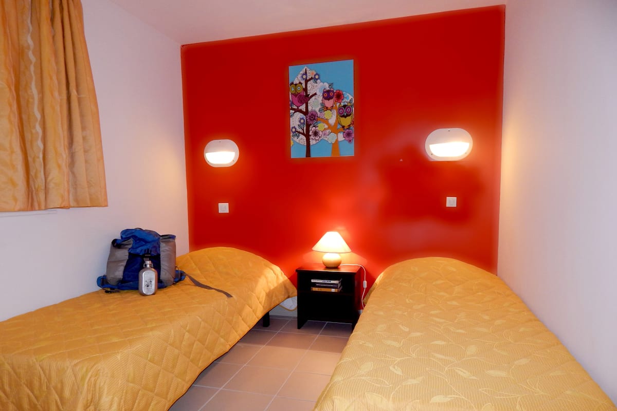 Ein Zimmer mit zwei Betten, einer roten Wand, einem Gemälde und einer Lampe.