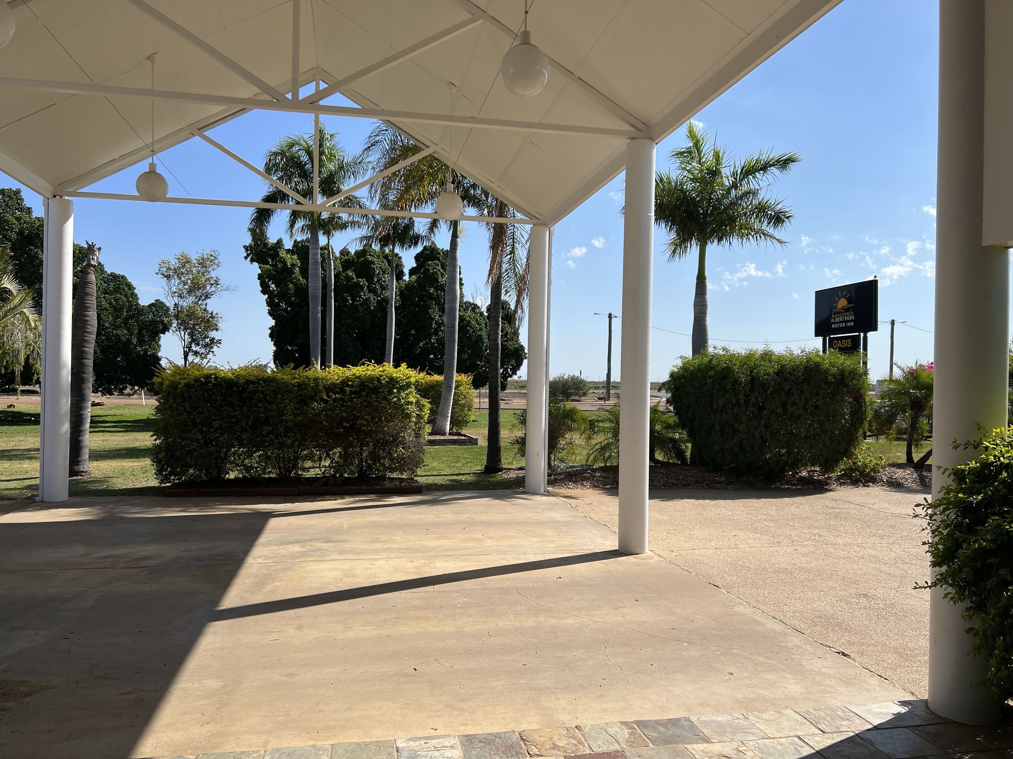 Un espacio al aire libre techado con palmeras y un cartel que indica OASIS Motor Inn.