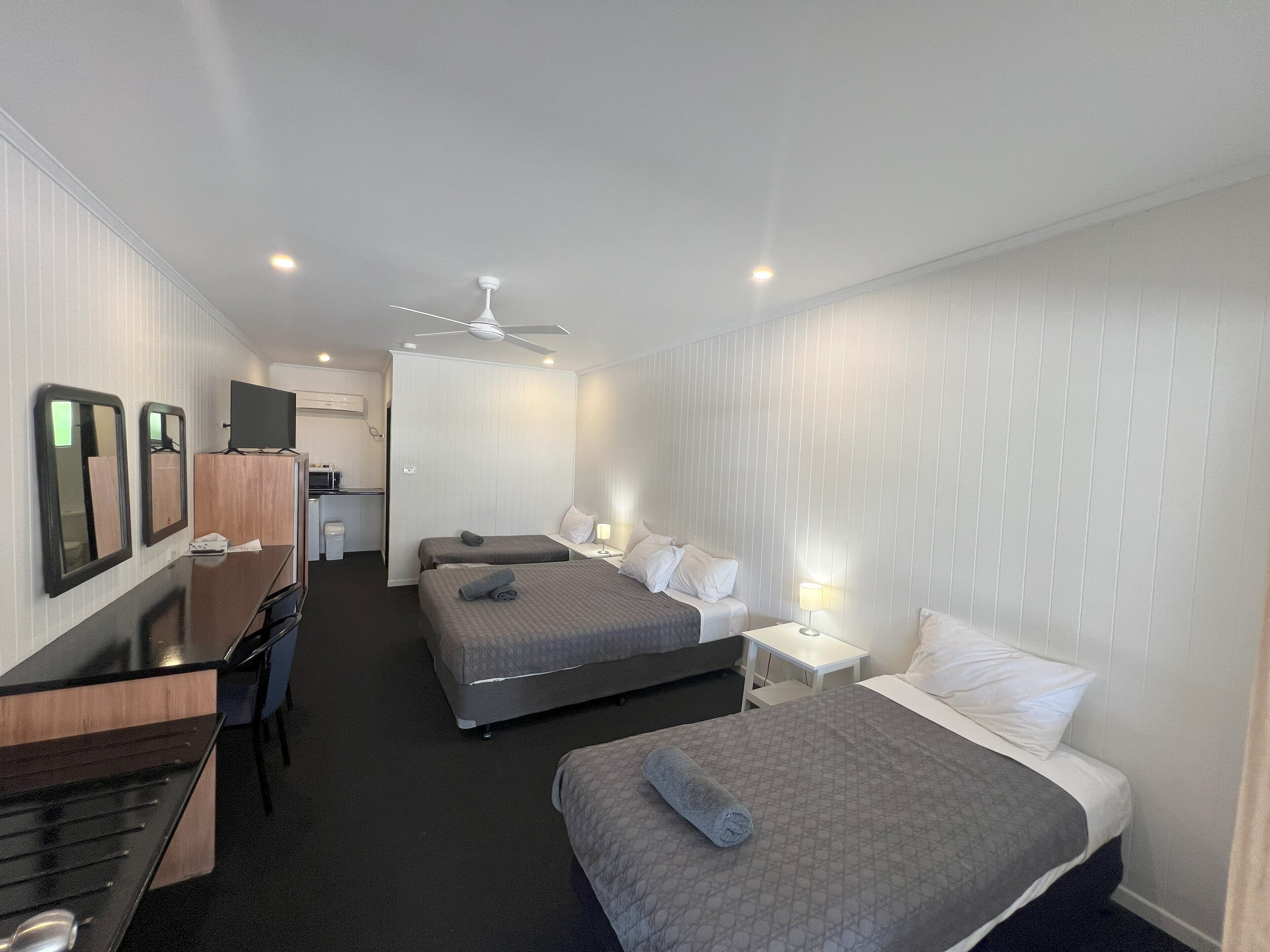 A hotel room with two beds, a desk, a chair, a TV, and a ceiling fan.