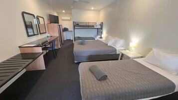 A hotel room with two beds, a desk, a chair, a TV, and a ceiling fan.