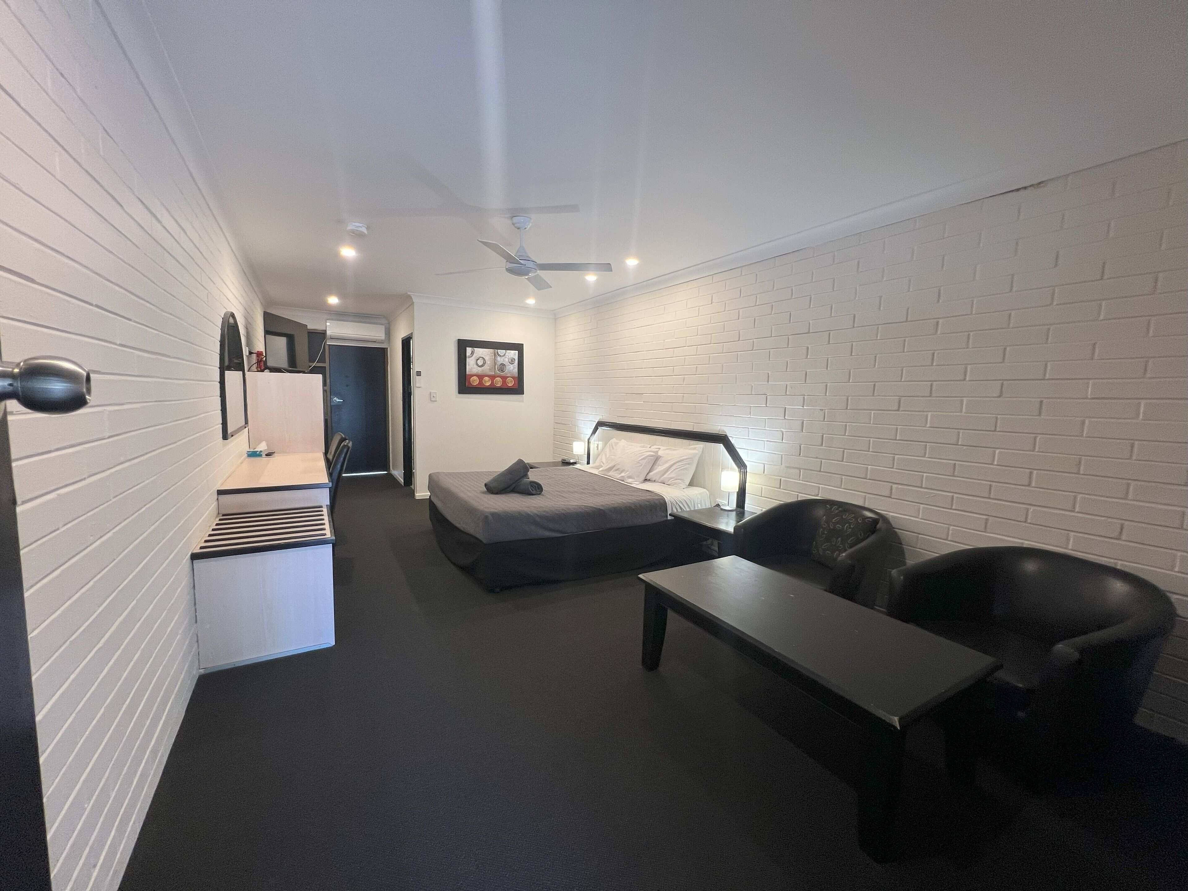 A compact hotel room with a bed, a desk, a chair, and a small table.