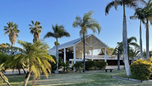 Un bâtiment moderne doté d’un patio couvert, entouré de palmiers et d’une pelouse verdoyante.